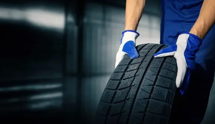 Mechanic holding new tire in a garage.