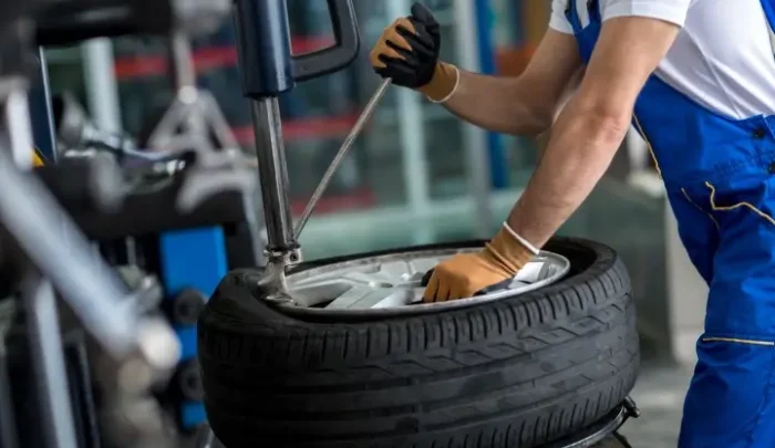 A man in blue overalls is repairing a tire, focused on his task in a workshop setting.